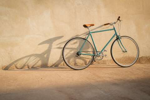 Teal bicycle leaning against a sunlit adobe wall